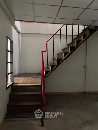 Industrial-style staircase with red railing in a minimalist interior space.