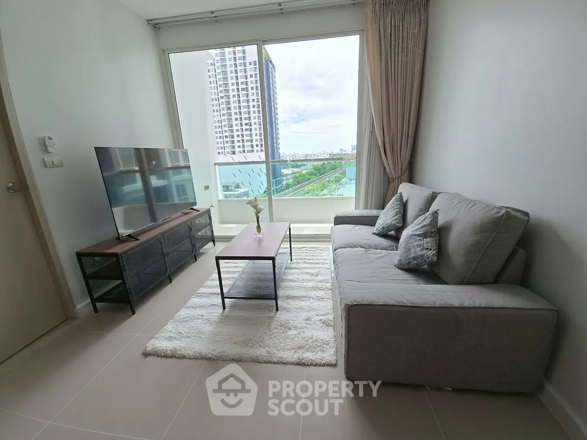 Modern living room with large window and city view, featuring a sleek sofa and flat-screen TV.