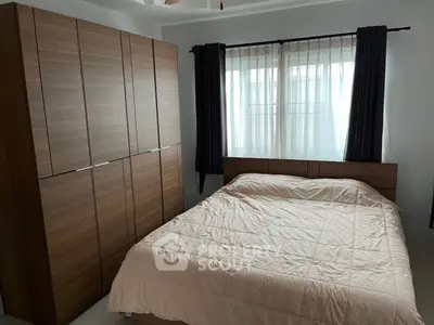 Cozy bedroom with large wardrobe and natural light through window curtains.