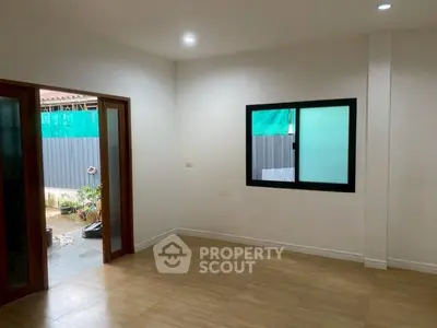 Spacious empty room with wooden flooring and sliding glass doors leading to a small outdoor area.