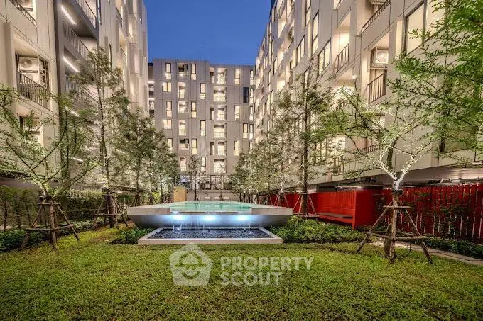 Modern apartment building with lush garden and stylish water feature at dusk.