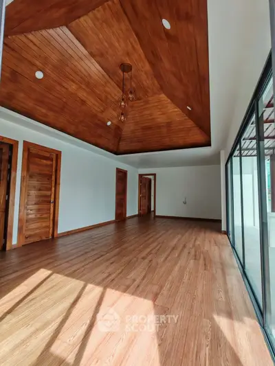 Spacious room with wooden ceiling and floor, large windows for natural light.