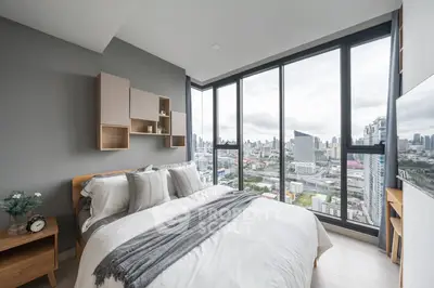Modern bedroom with stunning city view and floor-to-ceiling windows in a high-rise apartment.