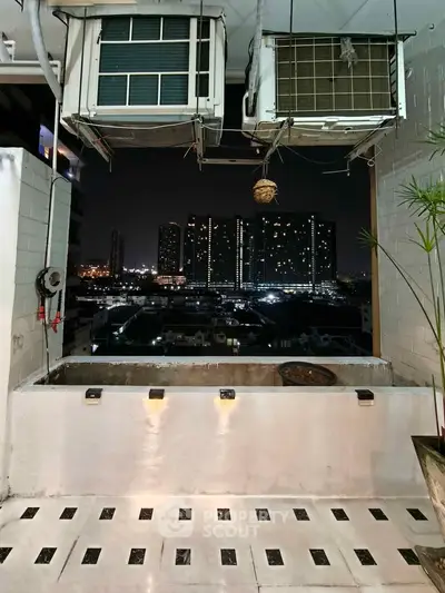 Stunning cityscape view from a modern balcony with ambient lighting and air conditioning units.