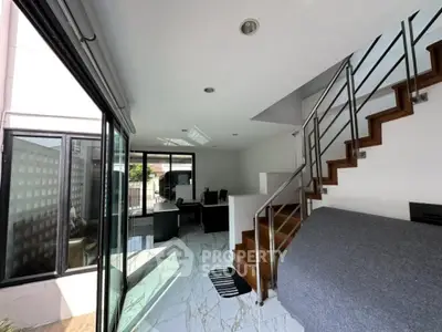 Modern living room with staircase and large windows, featuring sleek design and abundant natural light.