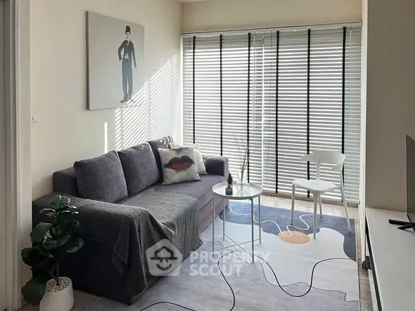 Cozy living room with modern decor, featuring a plush sofa, stylish rug, and large windows with blinds.