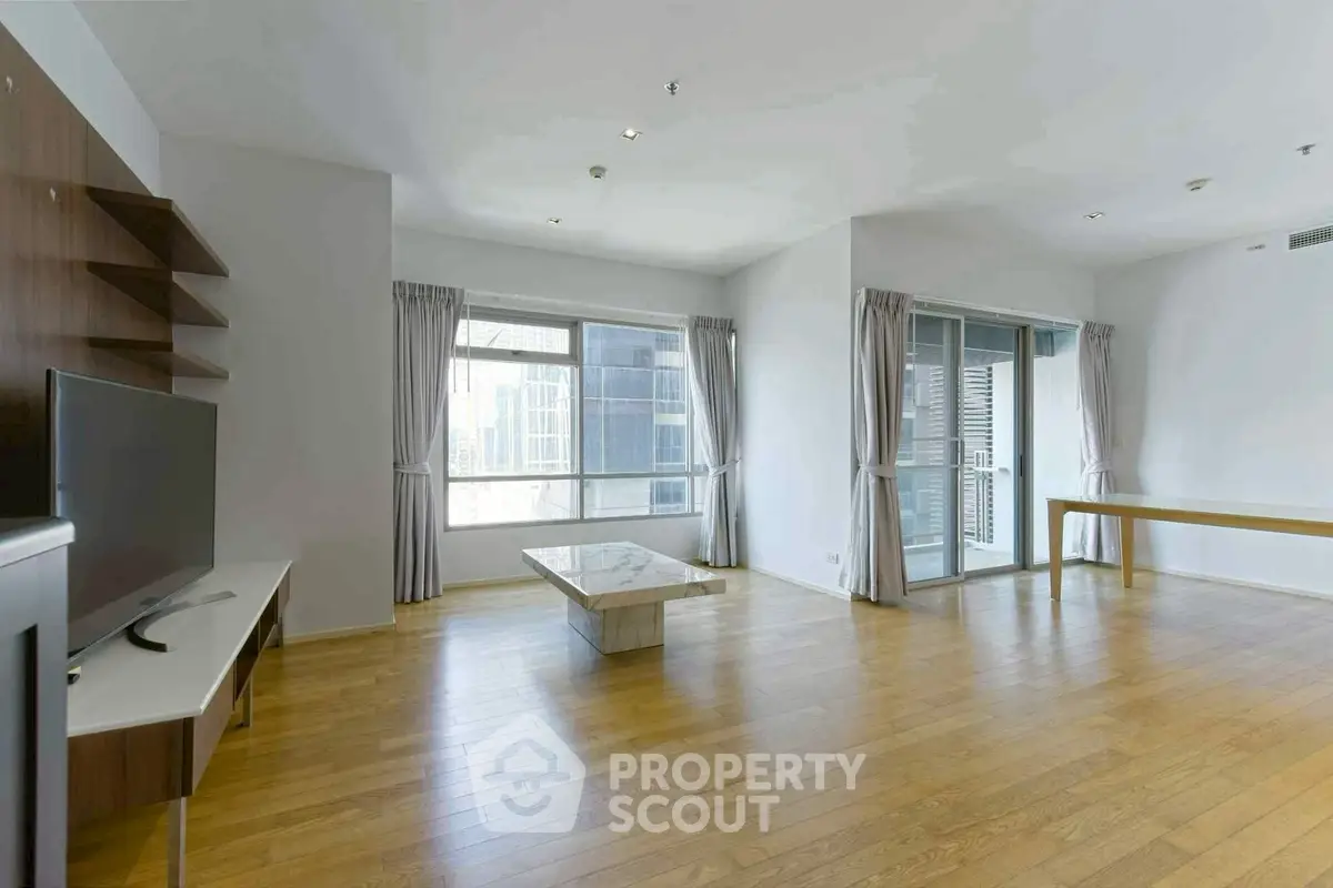 Spacious modern living room with wooden floors and large windows in a high-rise apartment.