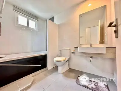 Modern bathroom with sleek fixtures, a large mirror, and a bathtub, complemented by natural light from the window.