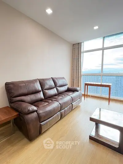 Spacious living room with leather sofa and panoramic city view from large window.