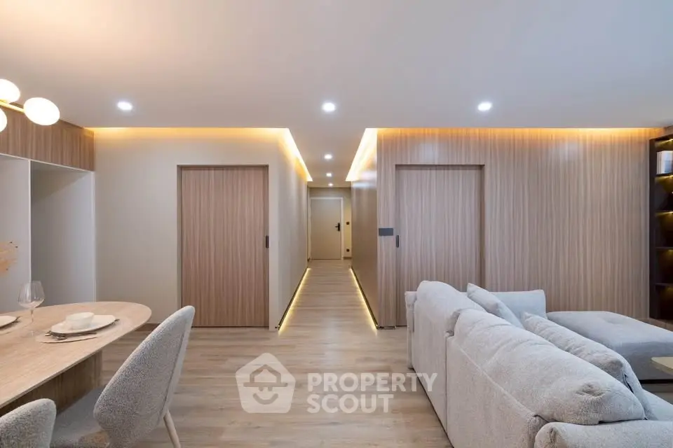 Modern living room with cozy seating and elegant dining area, featuring warm lighting and sleek wooden accents.