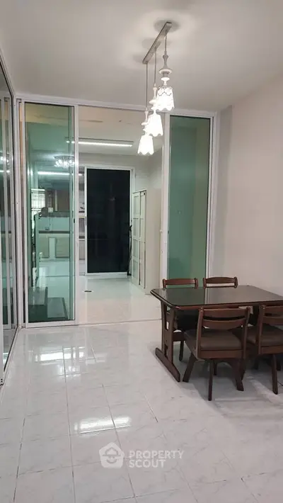 Spacious dining area with elegant lighting and glass doors leading to a modern kitchen.