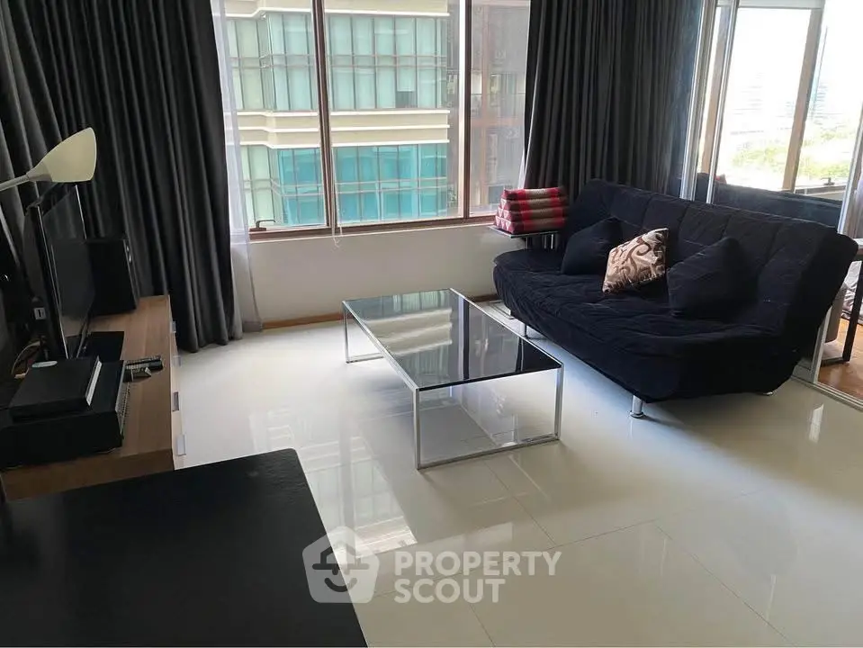 Modern living room with sleek black sofa and glass coffee table, large windows with city view.