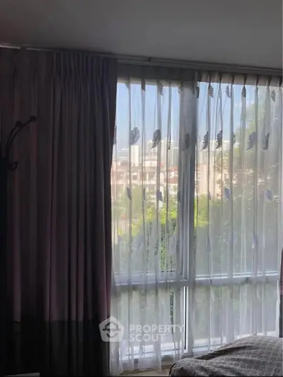 Cozy bedroom with large window and elegant curtains offering a serene city view.