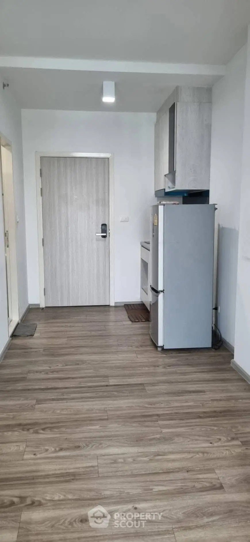 Modern apartment entrance with sleek wooden flooring and compact kitchen area.
