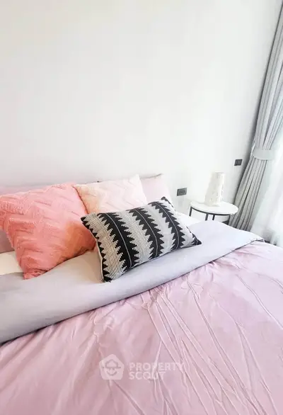 Cozy bedroom with stylish pillows and soft pastel bedding in a bright, modern apartment.