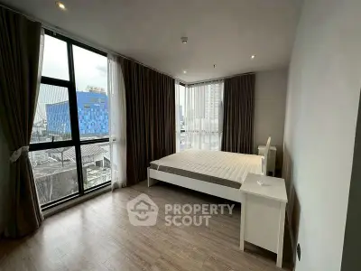 Spacious bedroom with large windows and modern decor in urban apartment.