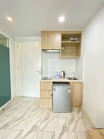 Compact modern kitchenette with wood cabinets and mini fridge in stylish apartment.
