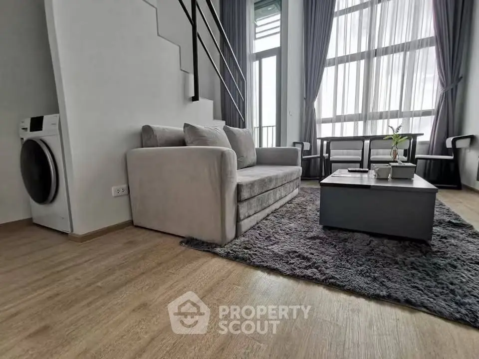 Modern living room with high ceilings and large windows, featuring a cozy sofa and stylish decor.