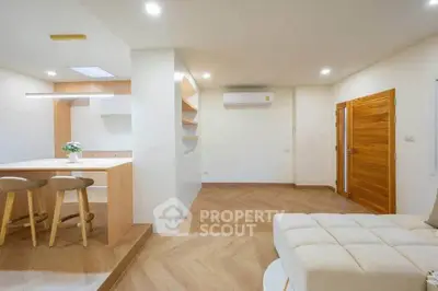 Modern open-plan living room with stylish kitchen and cozy seating area, featuring wooden accents and bright lighting.