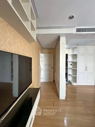 Spacious living room with elegant built-in storage and modern TV setup, featuring warm wooden flooring.