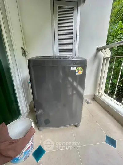 Spacious balcony with modern washing machine and lush greenery view.