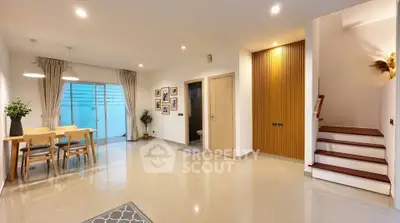 Spacious modern living area with dining set and staircase, featuring elegant decor and ample natural light.