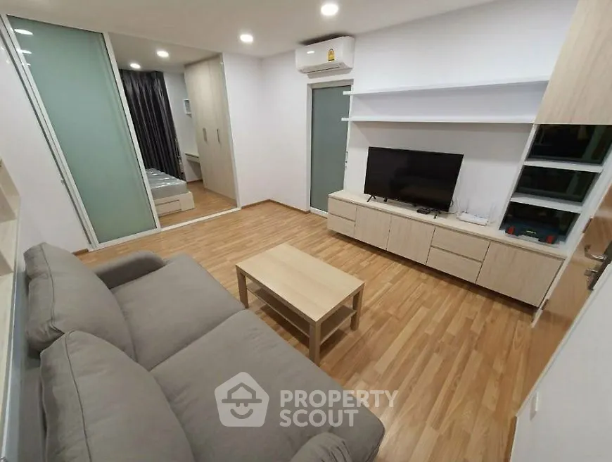 Modern living room with sleek design, featuring a cozy sofa, wooden flooring, and a flat-screen TV.
