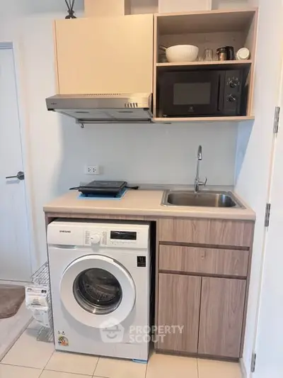 Compact kitchen with washing machine and microwave in modern apartment