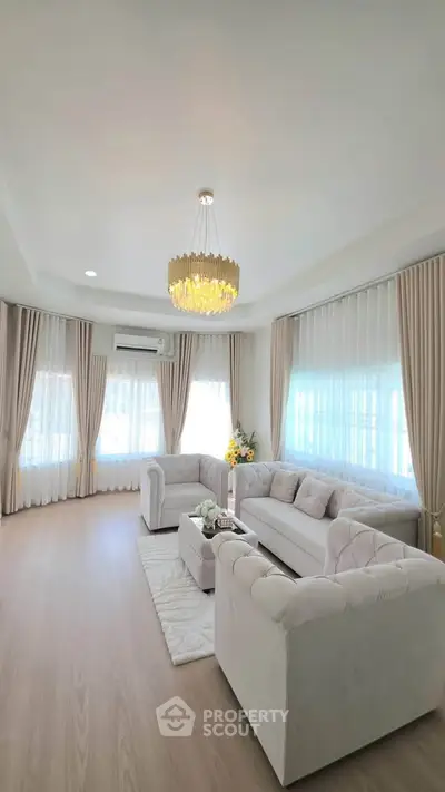 Elegant living room with plush sofas, chandelier, and large windows with sheer curtains.