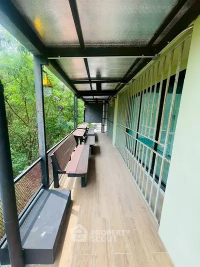 Spacious balcony with wooden benches and lush green view, perfect for relaxation.