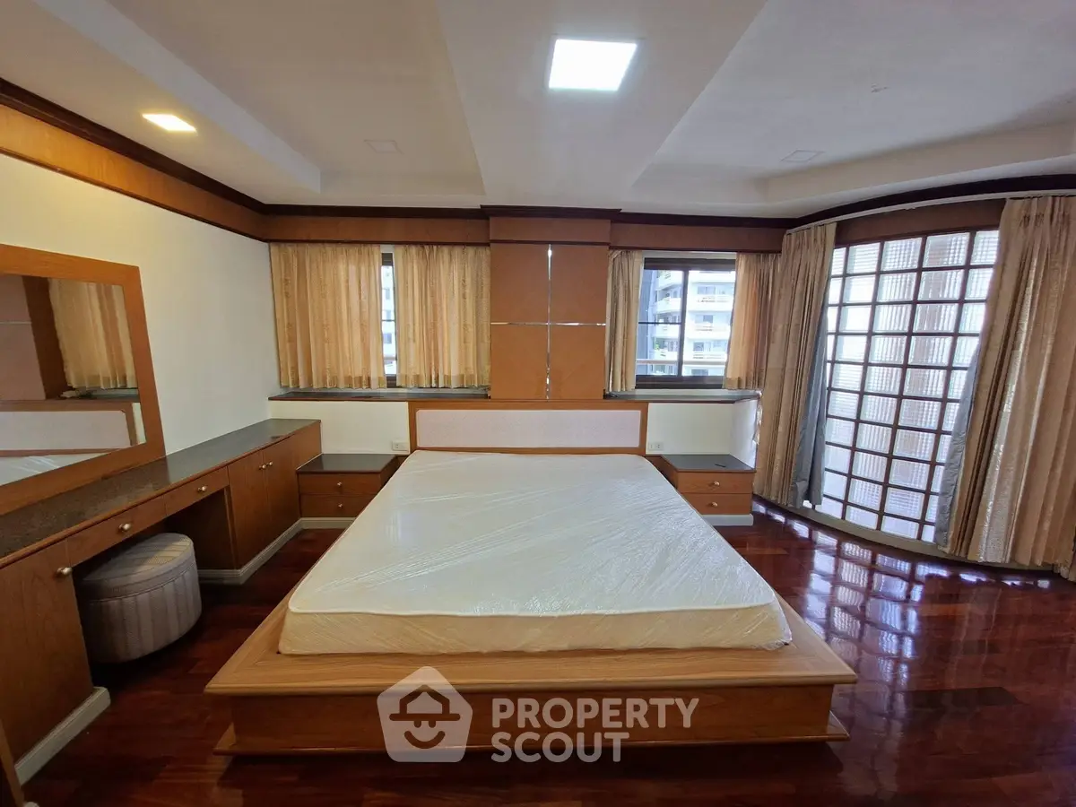 Spacious bedroom with elegant wooden furnishings and large windows for natural light.
