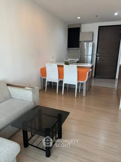 Modern open-layout living room with kitchen, featuring sleek furniture and wooden flooring.