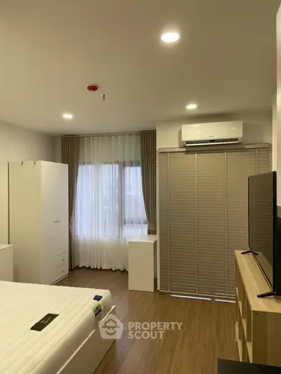 Modern bedroom with wooden flooring, air conditioning, and ample natural light from large windows.