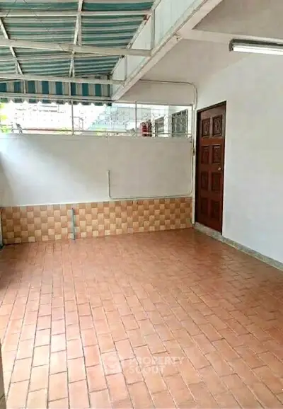 Spacious tiled patio with covered roof and wooden door, ideal for outdoor gatherings.