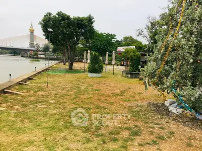Scenic riverside property with lush greenery and bridge view, ideal for development or leisure activities.