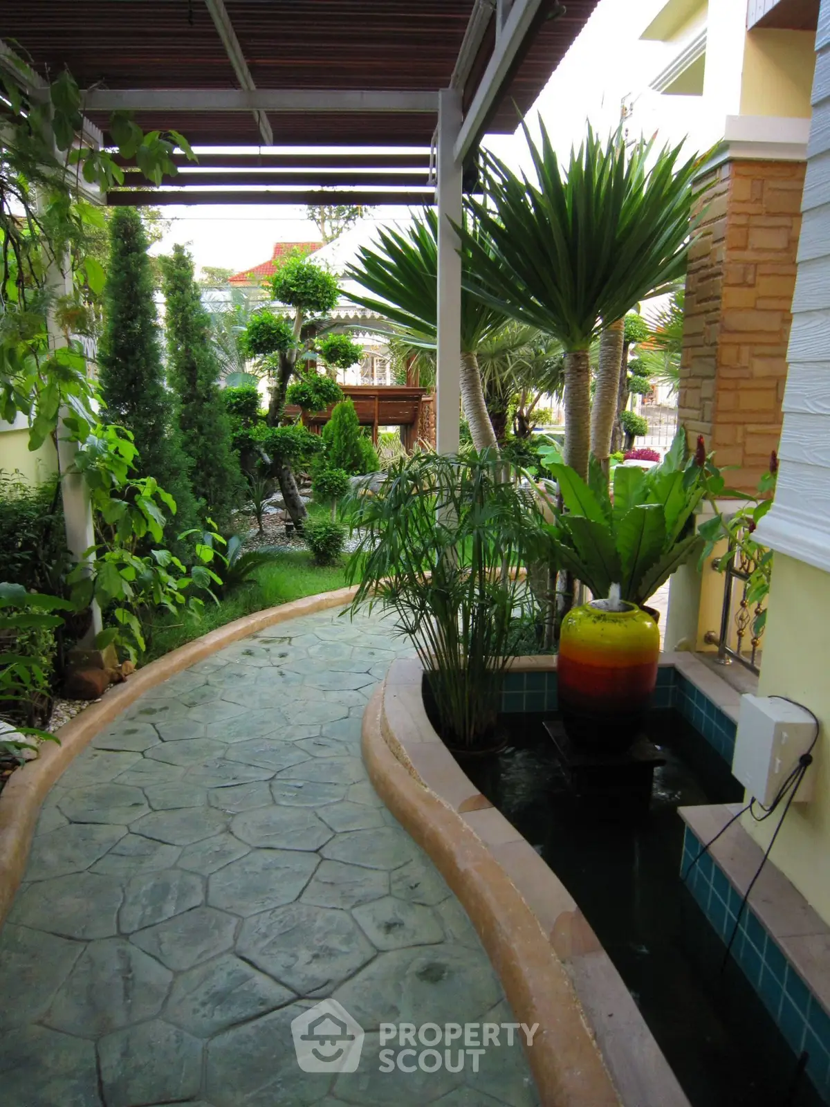 Charming garden pathway with lush greenery and decorative water feature in a serene residential setting.