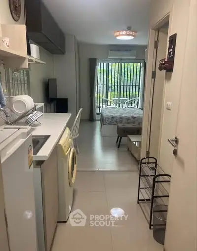 Modern compact apartment with open kitchen and cozy bedroom, featuring a washing machine and bright natural light.