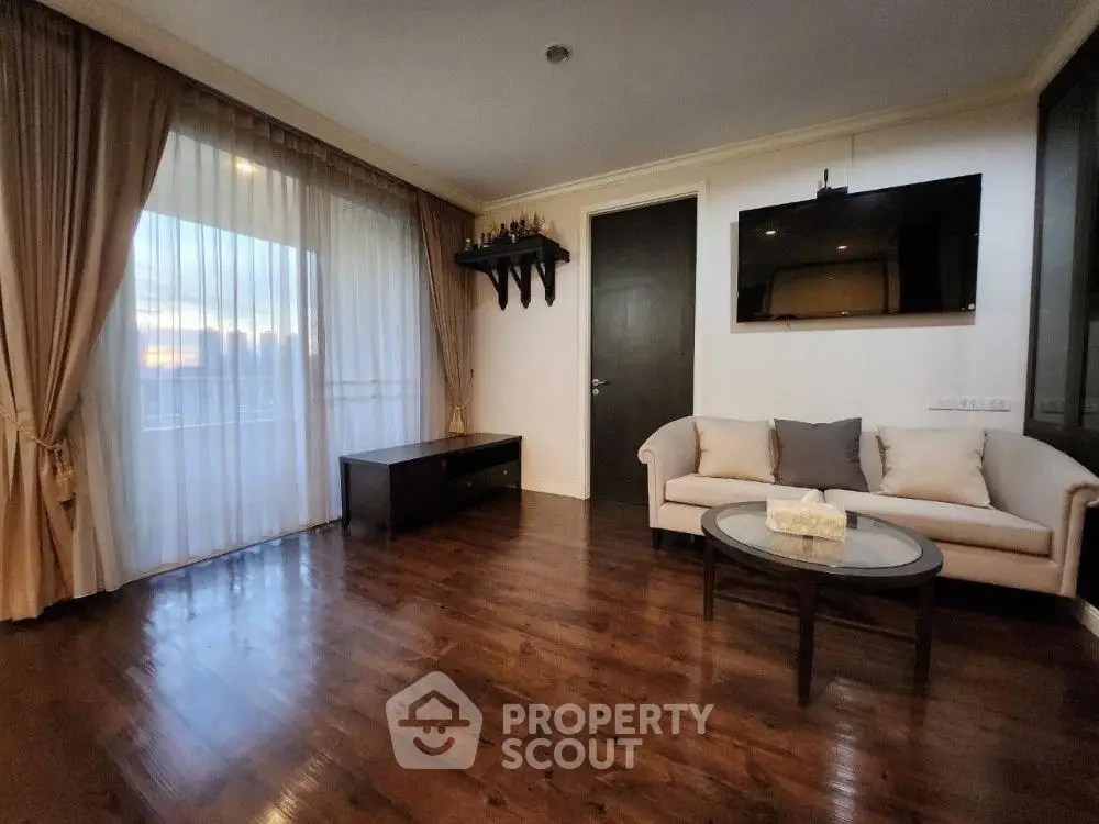 Spacious living room with elegant hardwood floors and modern decor, featuring a wall-mounted TV and large window.