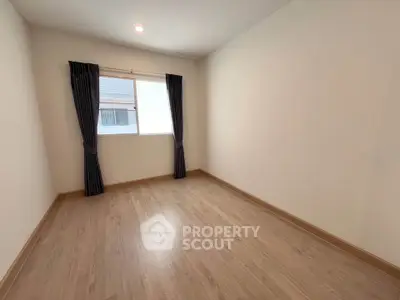 Spacious empty room with wooden flooring and large window, perfect for customization.