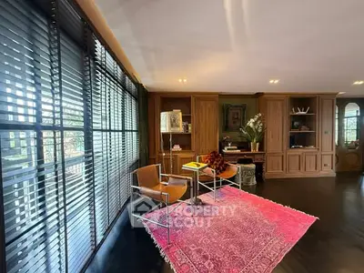 Elegant living room with wooden cabinetry and large windows, featuring a vibrant pink rug.