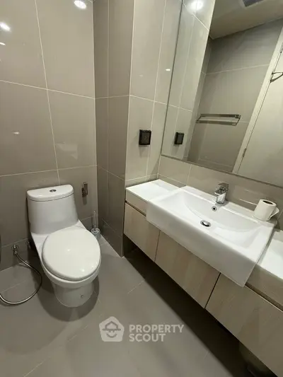 Modern bathroom with sleek fixtures and neutral tones, featuring a spacious sink and toilet.