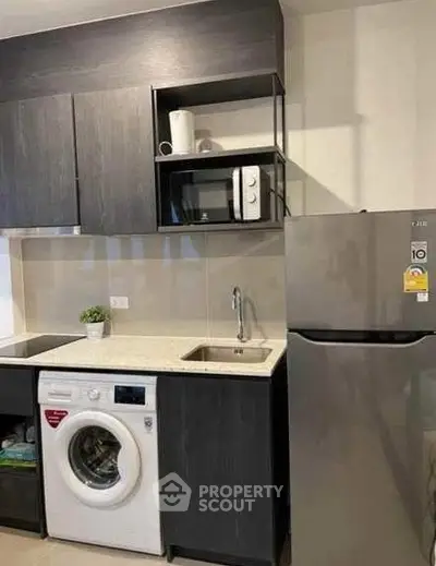 Modern kitchen with sleek cabinets, washing machine, microwave, and fridge.