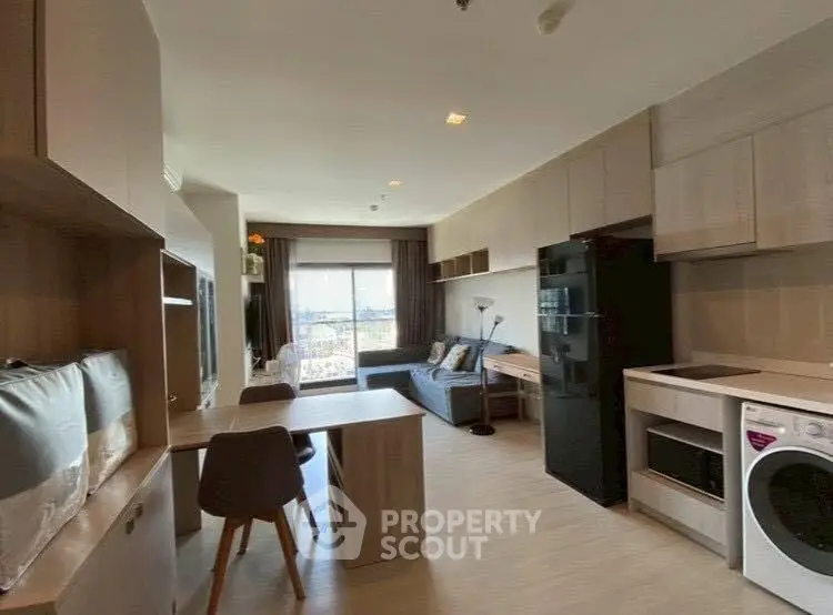 Modern open-plan living room and kitchen with stylish furniture and appliances, featuring a washing machine and fridge.