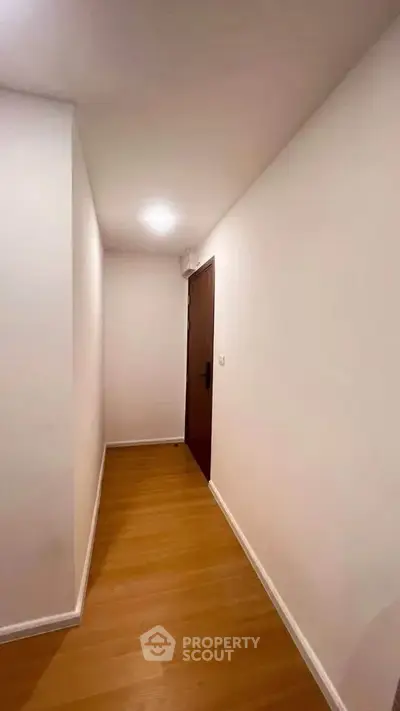 Minimalist hallway with wooden flooring and white walls leading to a wooden door.