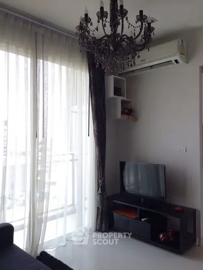 Elegant living room with chandelier and balcony view, featuring modern TV setup and air conditioning.