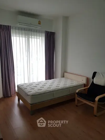 Cozy bedroom with single bed and natural light from large window.