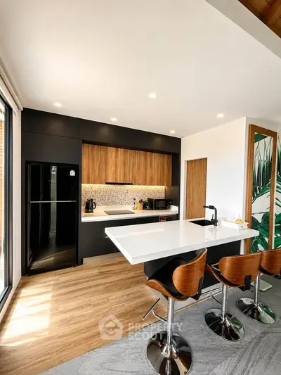 Modern kitchen with sleek black and wood cabinetry, island seating, and large windows for natural light.