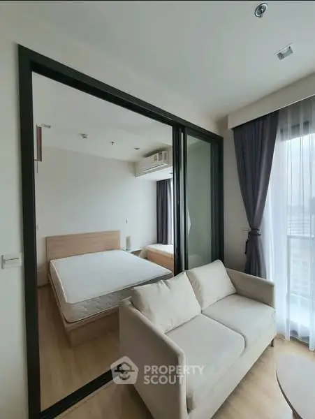 Modern apartment interior with cozy living room and bedroom separated by glass partition.
