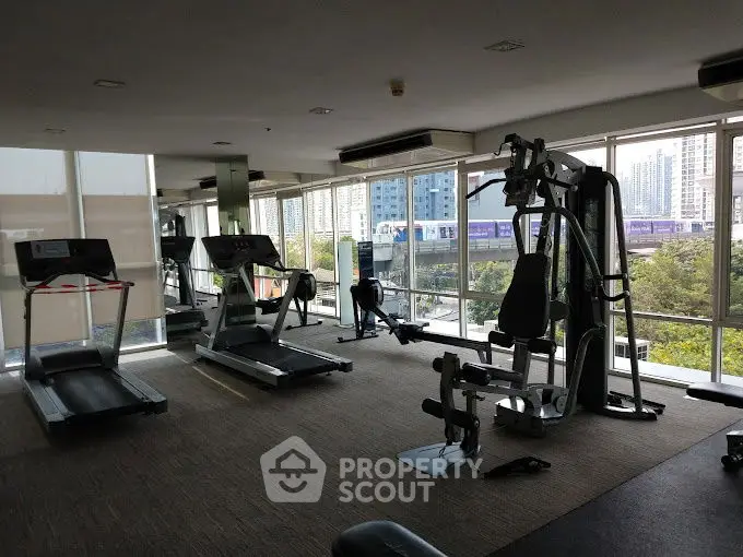 Spacious gym with modern equipment and city view in luxury apartment complex.