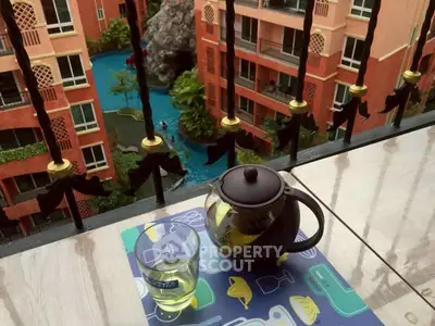 Charming balcony view with tea set overlooking vibrant pool area in modern apartment complex.